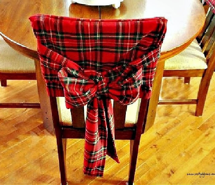 Red tartan Christmas chair cover tied with a large bow on the back of a wooden dining chair.