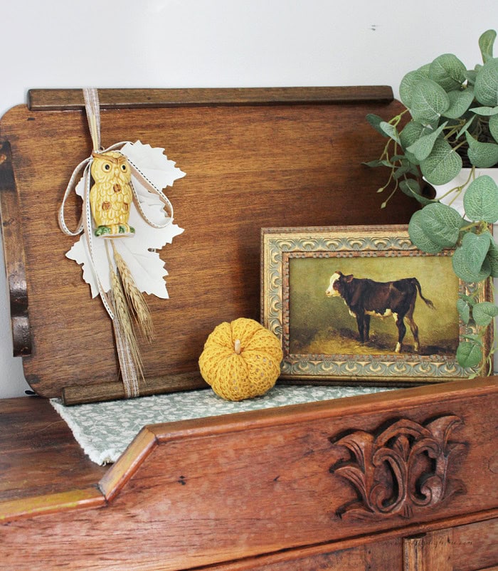 Fall decor with a vintage wood tray, owl salt shaker, cream leaves, pumpkin, framed cow print, and greenery.