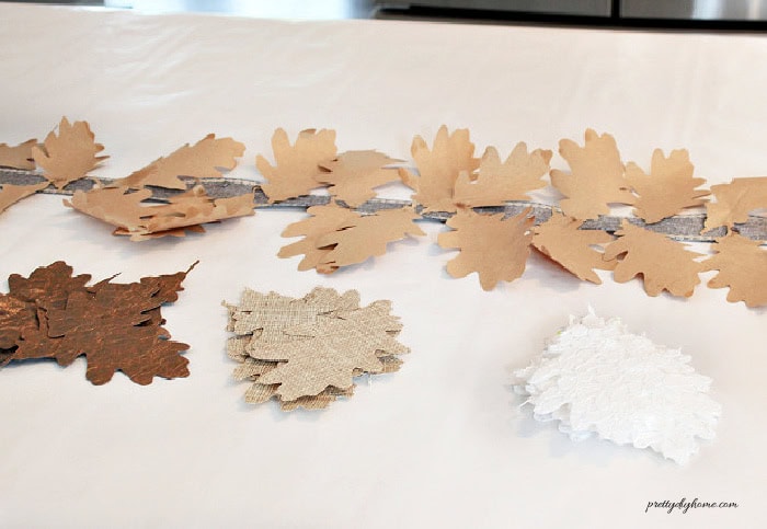 A fall leaf garland stretched across a long counter with stacks of dark brown, linen and lace oak leaves ready to add.