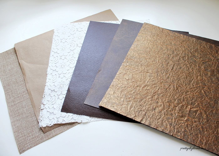 A selection of textured materials for a fall garland DIY, including white lace, coarse linen, brown paper and faux leather paper in warm autumn shades.