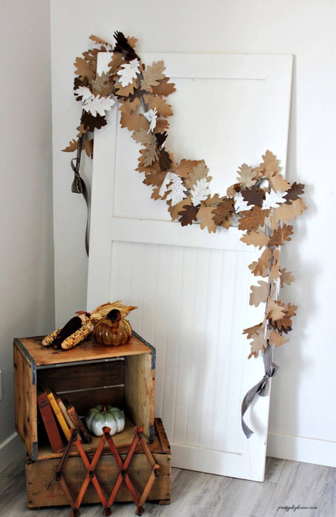 A fall garland DIY made with layered oak leaves in paper, lace and linen displayed on a white door.