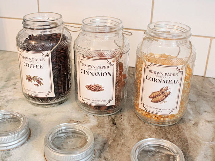 Three vintage pantry jars with printable labels are filled with coffee beans, cinnamon sticks, and cornmeal.