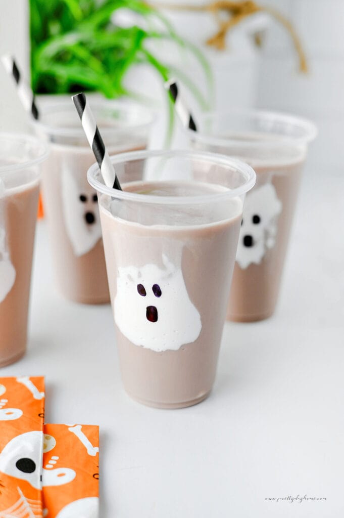 Ghost chocolate milk Halloween drink for kids with marshmallow fluff ghost in a clear cup.