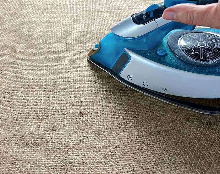 A steam iron pressing a piece of natural burlap fabric flat before cutting.