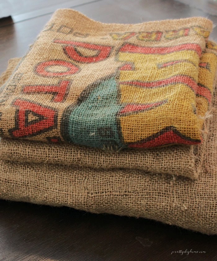Folded burlap fabric and a colorful vintage printed burlap sack stacked on a table