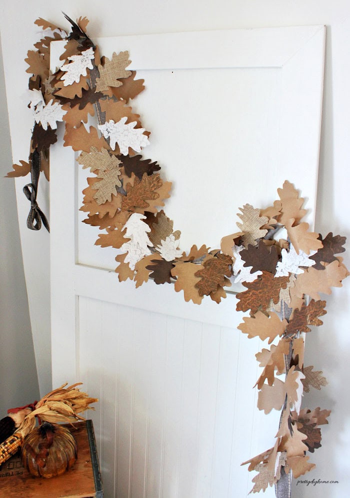 This close-up shows a mixed leaf fall garland made with layered oak leaves cut from brown paper, white lace, coarse linen, and textured faux leather paper.