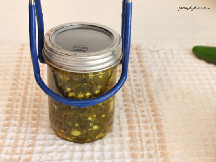 Placing a hot jar of cowboy candy on a towel-covered counter using a jar lifter.