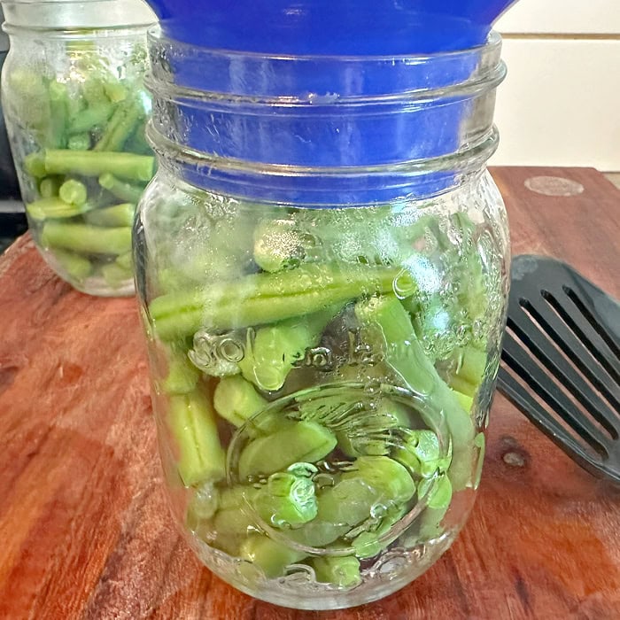 Hot green beans are being packed into warm canning jars before pressure canning.