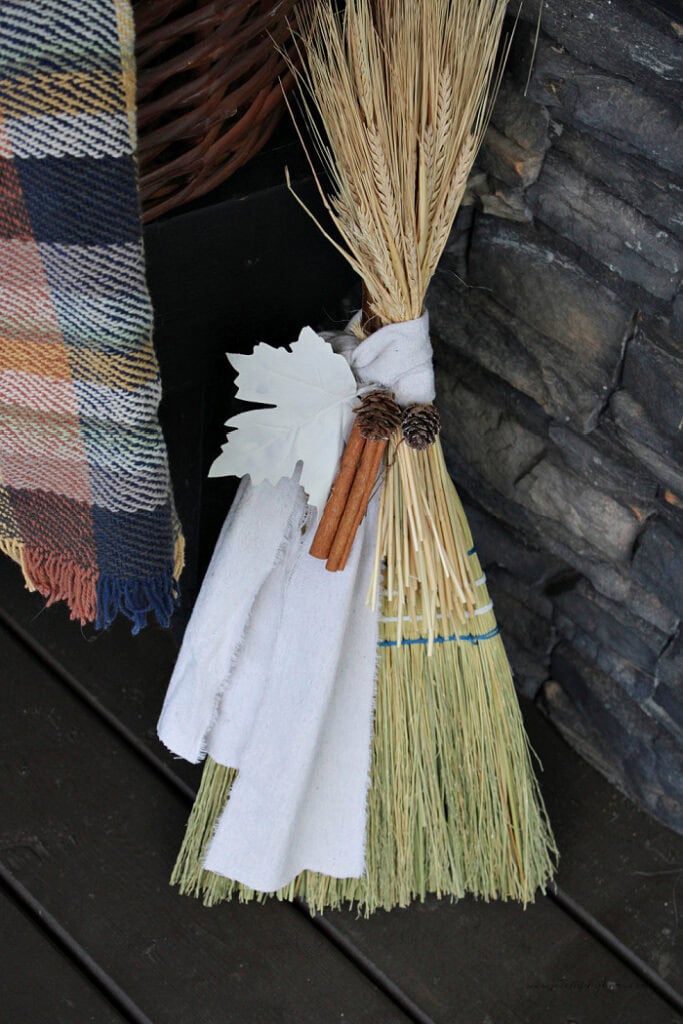 Primitive cinnamon broom fall decor with dried wheat, cinnamon sticks, pinecones, and warm white torn fabric.
