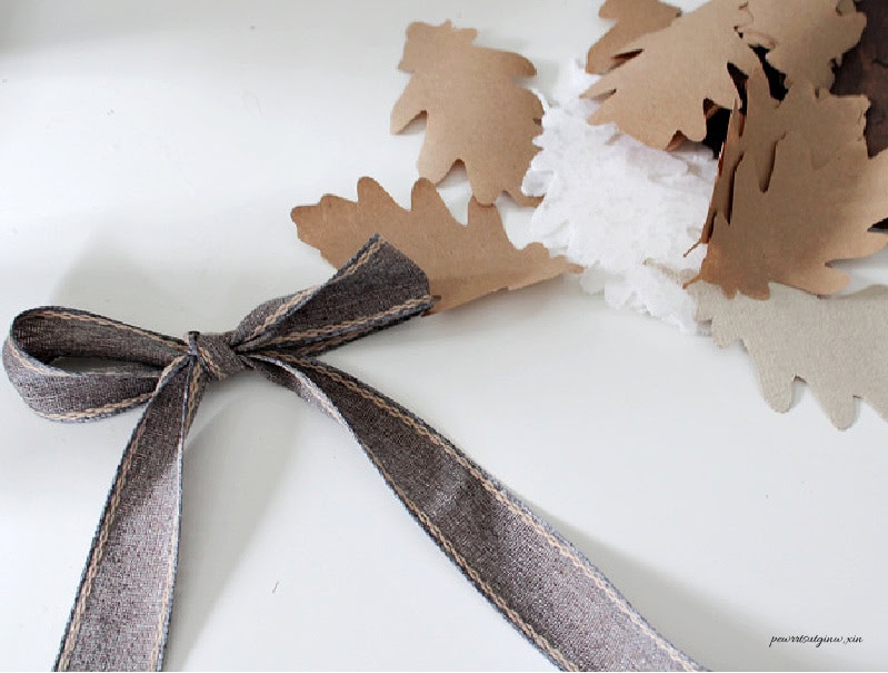 A ribbon bow is tied at the beginning of the fall garland beside layered oak leaves in paper, lace and linen.