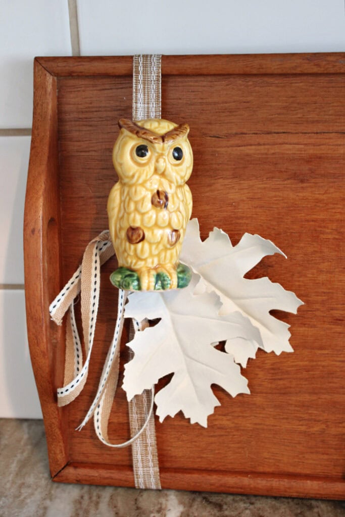Close-up of a vintage owl salt shaker on a fall wood tray with cream painted leaves and ribbon.