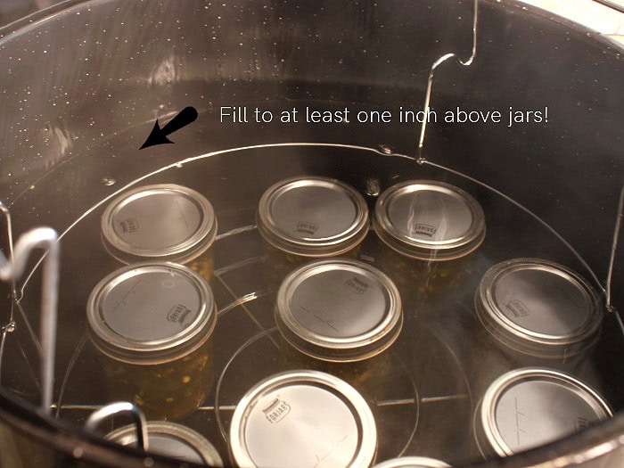 Cowboy candy jars processing in a water bath canner with water covering the jars.