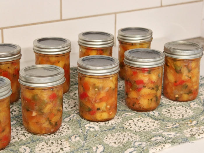 Homemade canned peach salsa in glass jars with peaches, red pepper, jalapeño, and cilantro.