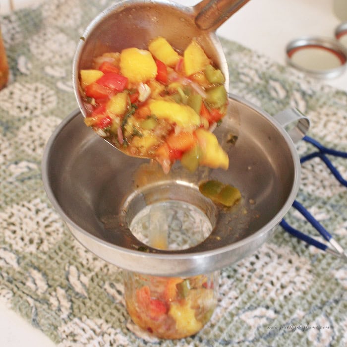 Ladling hot peach salsa through a canning funnel into a half-pint jar.