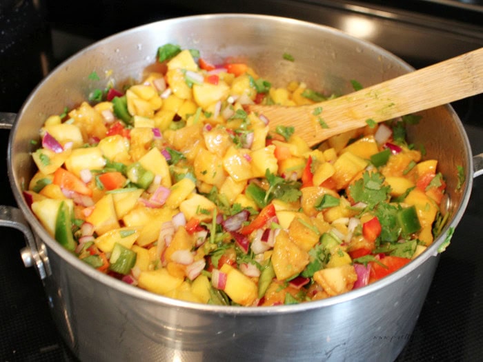 Chopped peaches, red onion, jalapeños, red pepper, and cilantro in a saucepan for peach salsa.