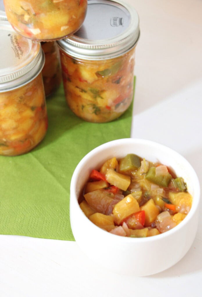 Homemade peach salsa served in a white bowl with jars of canned peach salsa in the background.