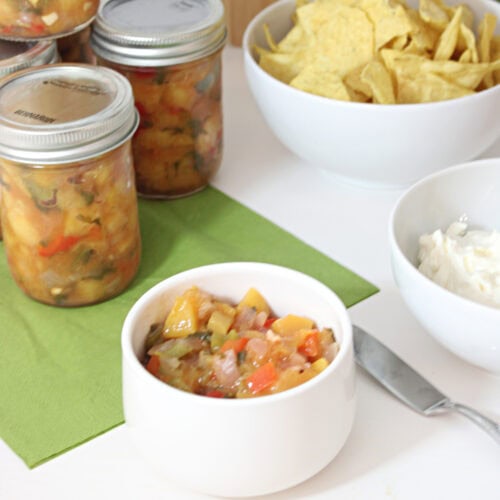 Homemade peach salsa served with tortilla chips beside jars of canned peach salsa.