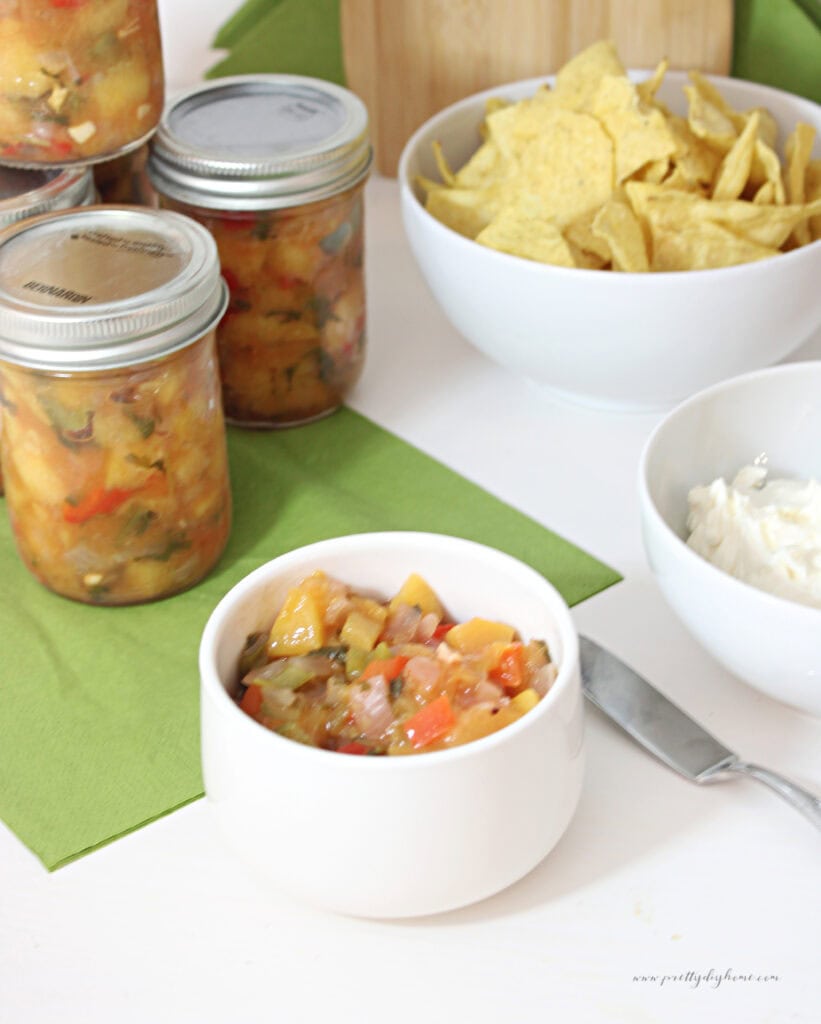 Homemade peach salsa served with tortilla chips beside jars of canned peach salsa.