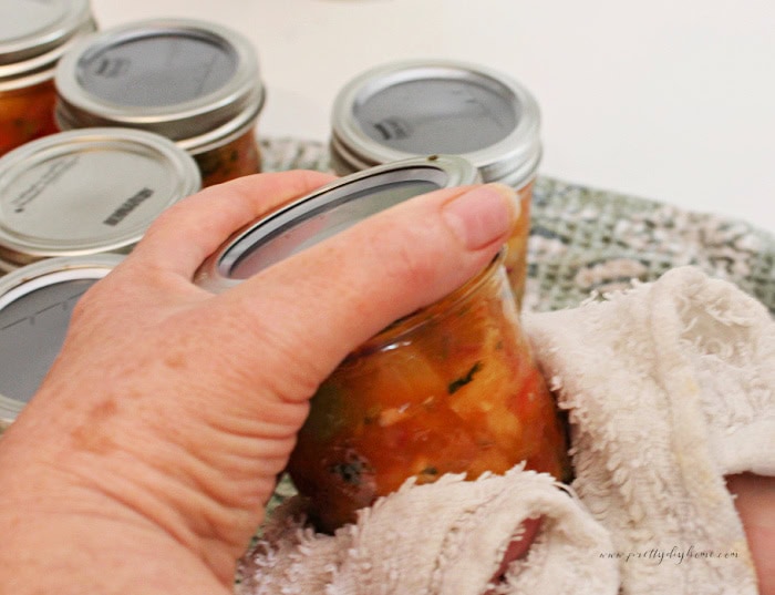 Tightening the screw band on a hot half-pint jar of homemade peach salsa.