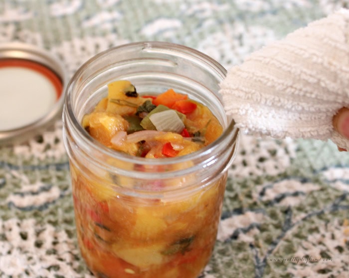 Wiping the rim of a jar filled with homemade peach salsa before adding the canning lid.