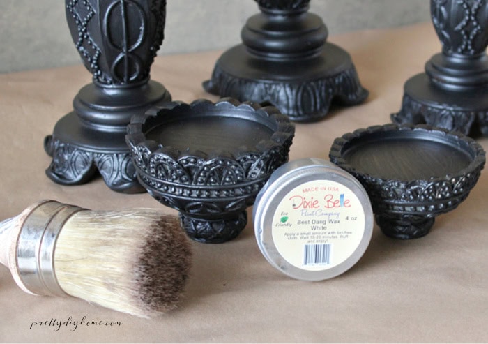 Black Halloween candlesticks beside white furniture wax and a wax brush before adding the ghostly finish.