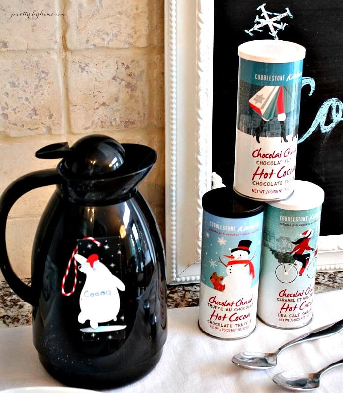 Christmas hot chocolate bar with cocoa tins, coffee carafe, and festive bear tag.