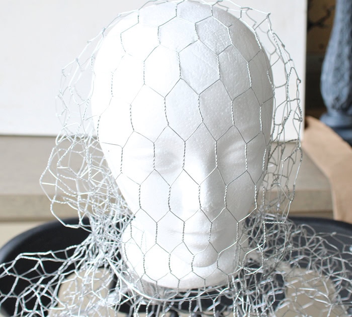 Chicken wire is shaped over a styrofoam head while building a DIY Halloween ghost.