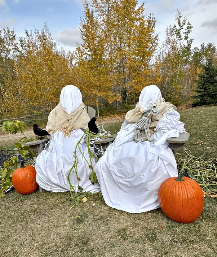 DIY outdoor Halloween ghost decorations made with white fabric, vintage shawls, pumpkins and crows.