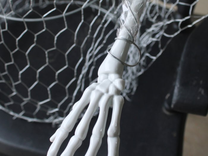 A plastic skeleton hand is secured to the wire arm of a DIY Halloween ghost.