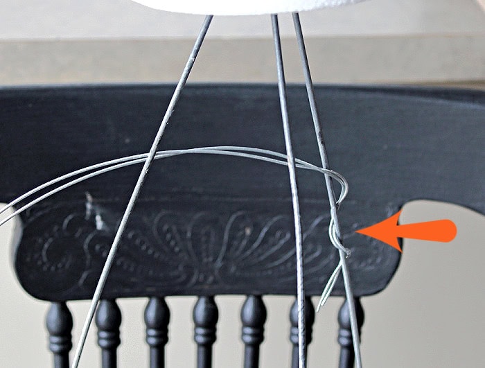 A wire arm is wrapped and secured to the tomato cage frame of a DIY Halloween ghost.