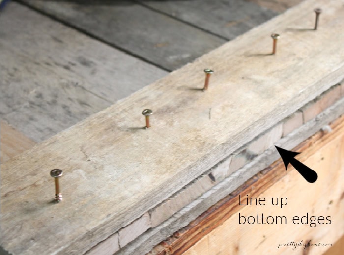 Screws placed along a pallet wood cross piece for assembling a DIY Halloween gravestone.