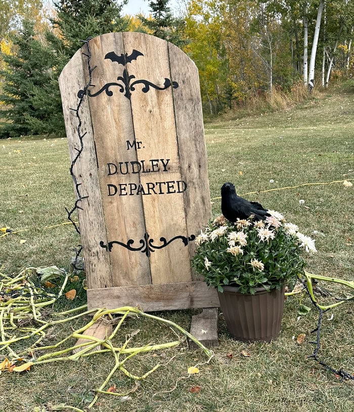 DIY wooden Halloween gravestone with painted bat scrollwork, flowers and a black crow.