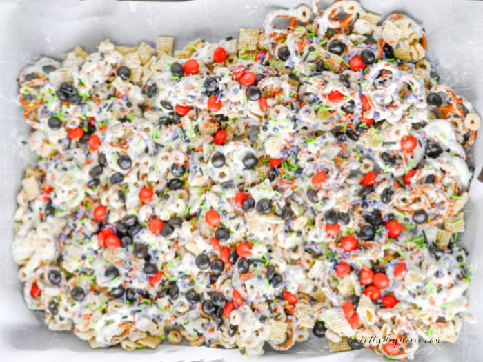 Halloween M&Ms and colorful sprinkles added over white chocolate coated cereal and pretzels for an easy Halloween party snack mix.