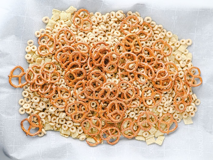 Rice Chex, Honey Nut Cheerios, and pretzels spread on a parchment lined baking sheet for an easy Halloween party snack mix.