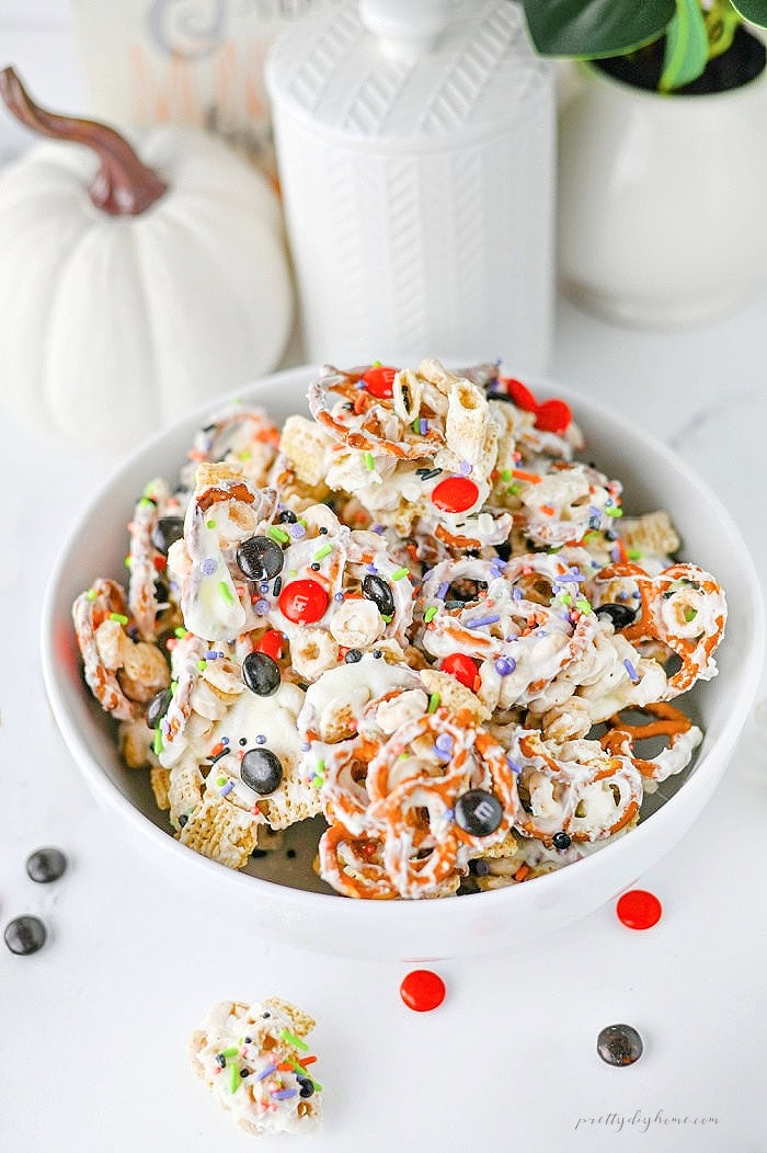 Ghost Crunch Halloween party snack mix with white chocolate cereal, pretzels, Halloween M&Ms, and colorful sprinkles in a white bowl.