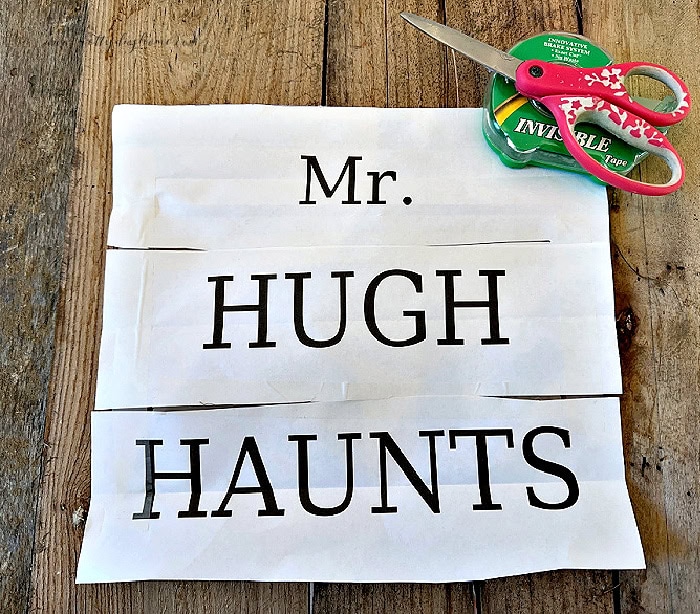 Printed Mr. Hugh Haunts lettering stencil pieces laid out on pallet wood for a DIY Halloween gravestone.