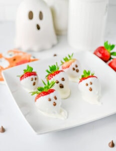 Halloween strawberry ghosts dipped in white chocolate with chocolate faces on a serving tray.