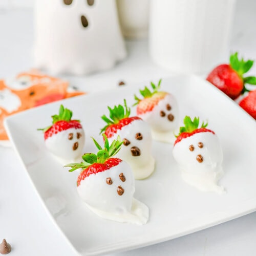 Halloween strawberry ghosts dipped in white chocolate with chocolate faces on a serving tray.