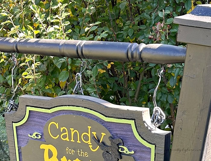 Finished DIY Halloween sign hanging from a wooden spindle with hooks and plastic chain.