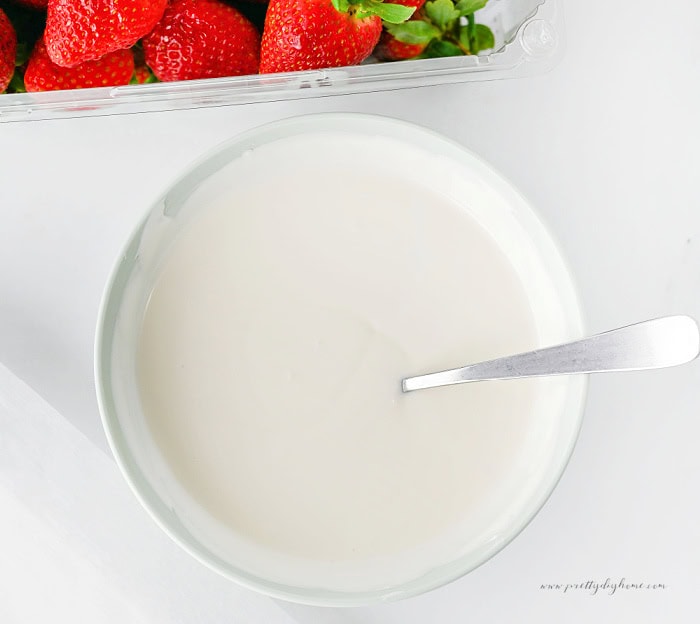 Melted vanilla almond bark in a bowl ready for dipping the strawberry ghosts.