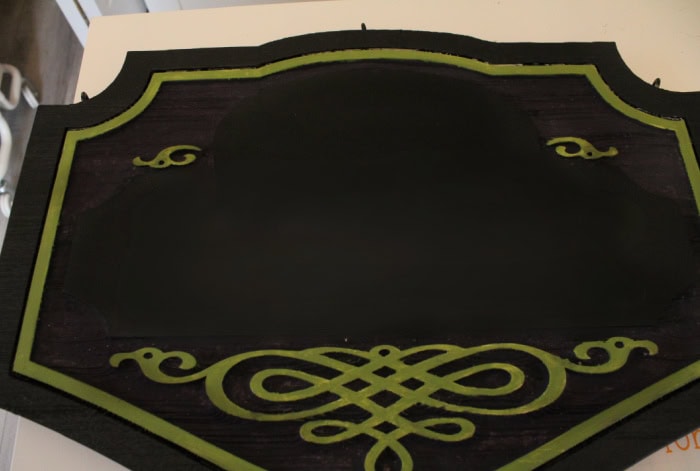 Painted Halloween sign with black, green, and dark purple details before adding vinyl lettering.