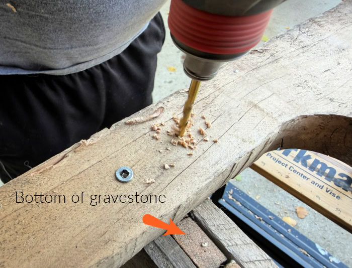 Predrilling a hole in pallet wood for the base support of a DIY Halloween gravestone.