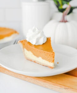 Slice of pumpkin cheesecake pie showing distinct pumpkin and cream cheese layers, topped with whipped cream