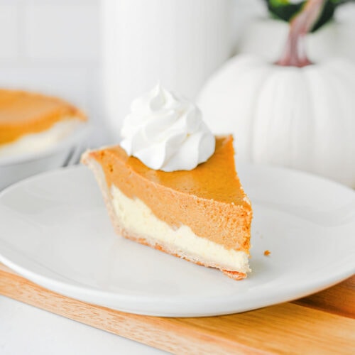 Slice of pumpkin cheesecake pie showing distinct pumpkin and cream cheese layers, topped with whipped cream