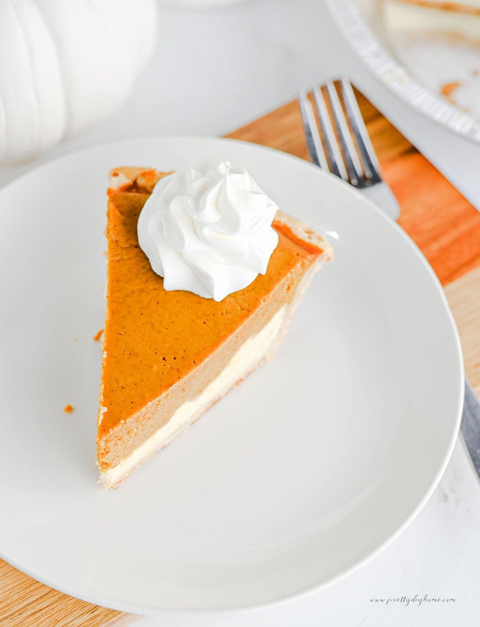 Slice of pumpkin cheesecake pie topped with whipped cream, showing separate pumpkin and cream cheese la