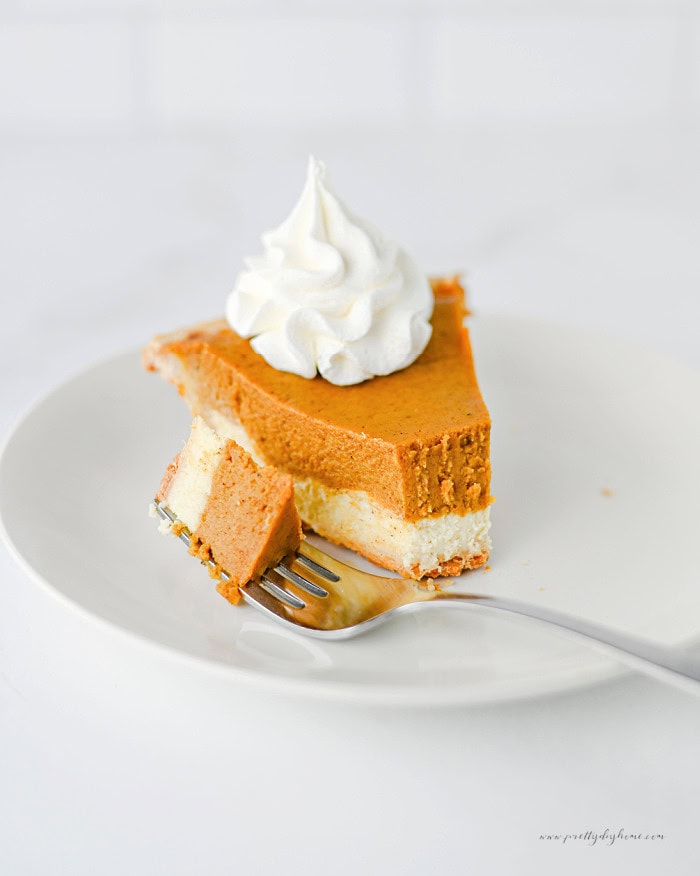 Pumpkin cheesecake pie topped with whipped cream, with a forkful showing the pumpkin and cream cheese layers.
