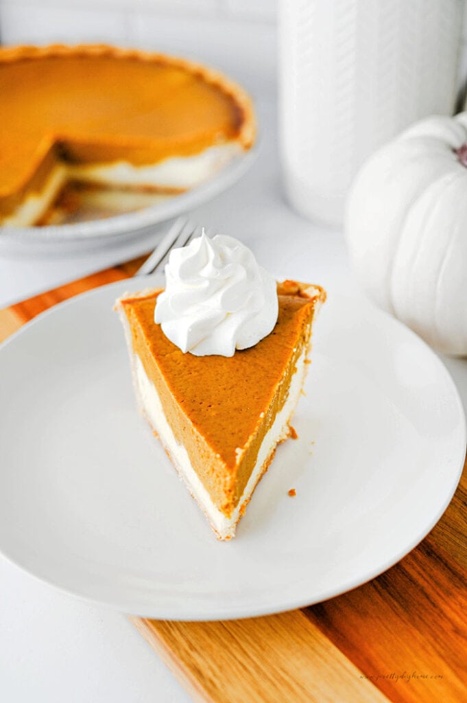 Slice of pumpkin pie cheesecake topped with whipped cream, showing the pumpkin and cream cheese layers.