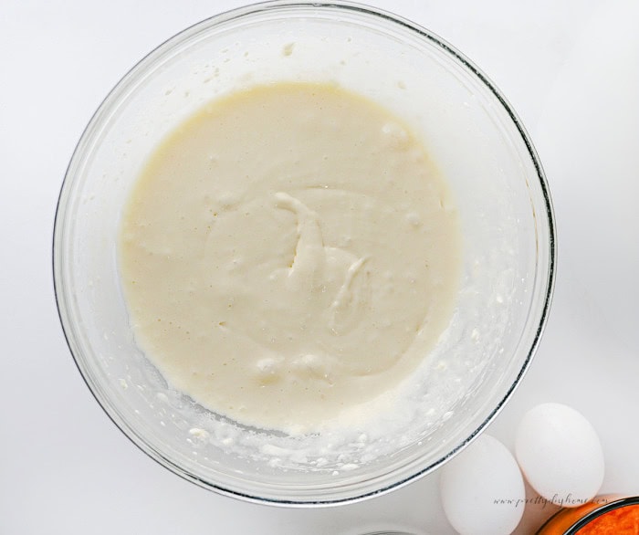 Cream cheese filling mixed until smooth in a glass bowl for pumpkin pie cheesecake.