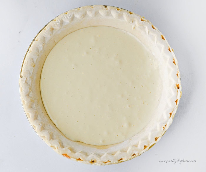 Cream cheese layer spread inside a prepared pie crust for pumpkin pie cheesecake.