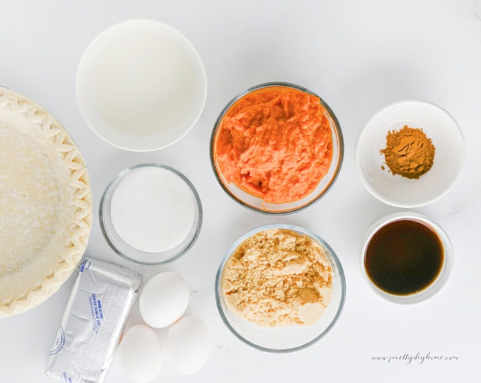 Ingredients for pumpkin pie cheesecake including pumpkin puree, cream cheese, eggs, sugar, cream, vanilla, pumpkin pie spice, and pie crust.
